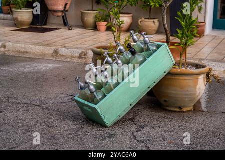 Ten old soda water bottles in a green wooden box in front of a bar as decoration. Stock Photo