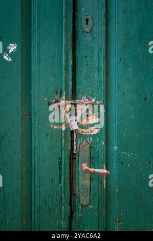 Old weathered entrance door painted green, secured with a chain and padlock. Stock Photo