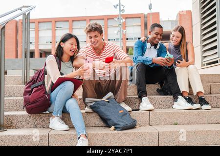 Group of university students sitting on outdoor stairs, laughing and using smartphones together, enjoying social media and online interaction during a break from their studies at campus. High quality photo Stock Photo