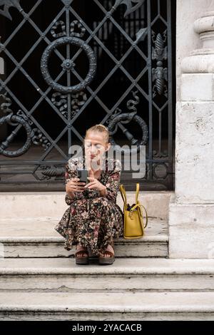 Vicenza, Italy - August 12 2024: Italian Woman Sitting on Stairs of the Loggia del Capitaniato and Reading on her Smartphone. Stock Photo