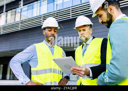 Construction site manager using tablet while having a discussion with colleagues Stock Photo