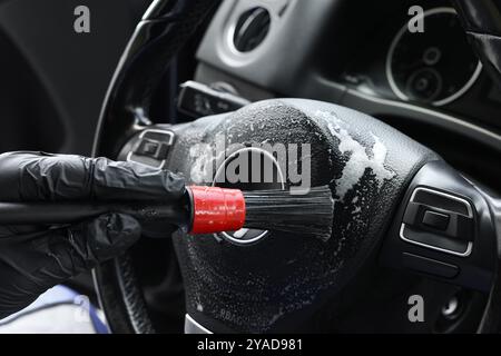 Man cleaning steering wheel with brush in car, closeup Stock Photo
