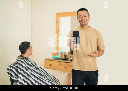 A man gets his hair cut by a barber while using a cell phone Stock Photo
