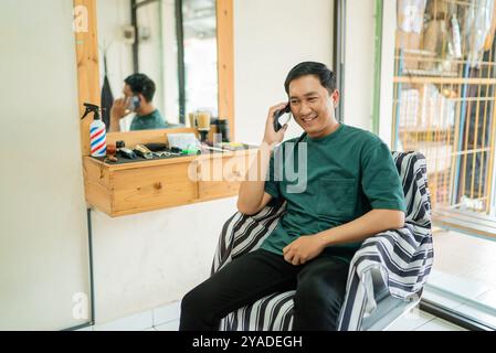 A man sits in a barber shop chair talking on a cell phone Stock Photo