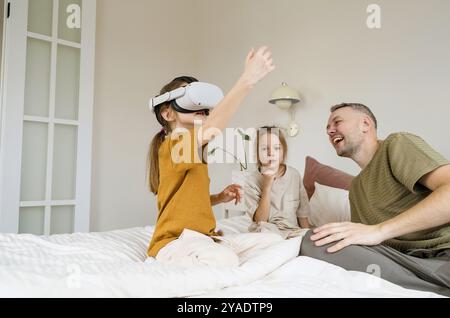 A young girl wearing a VR headset is immersed in the virtual world, reaching out with her hand as if to touch something. Stock Photo