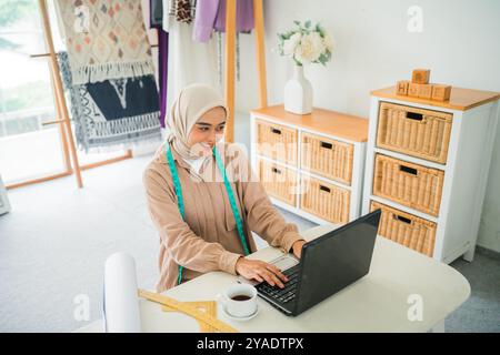An Elegant Seamstress is Working on a Laptop in a Modern Studio Environment Stock Photo