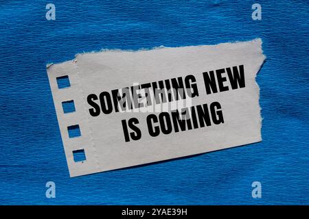 Something new is coming message written on ripped torn paper piece with blue background. Conceptual something new is coming symbol. Copy space. Stock Photo