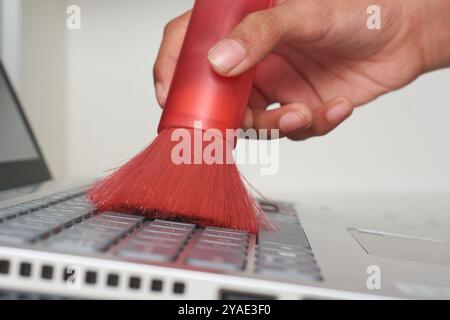 cleaning laptop keyboard with soft bristle brush in close-up view, remove dust and debris from computer components in selective focus with copy space Stock Photo