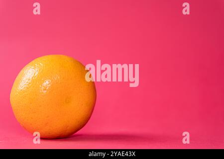 A single orange placed on a vibrant pink background, showcasing its round shape and texture. The bright colors create a striking contrast, emphasizing Stock Photo