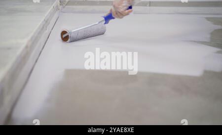 Construction worker wearing protective gloves applying epoxy resin on the floor using a roller. Stock Photo