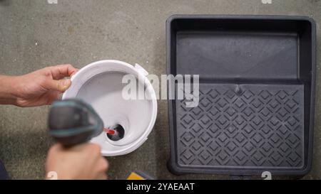 Construction worker is mixing white paint in a bucket using an electric drill and a paint mixer attachment Stock Photo