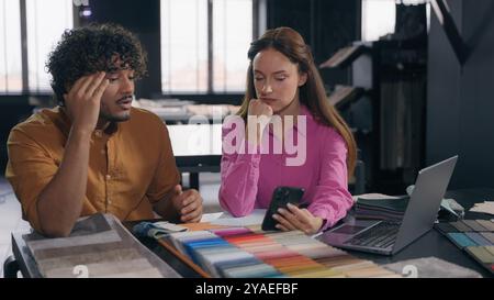 Two designers male female colleagues in modern design studio looking at fabric samples discussing color textile for interior angry Arabian Indian man Stock Photo