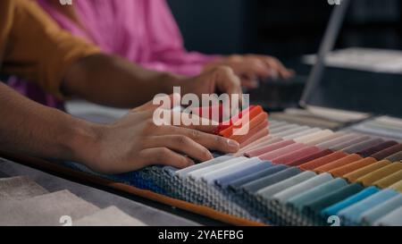 Close up details woman assistant and man designer choosing color fabric samples hands touch textile swatches velvet upholstery material for furniture Stock Photo