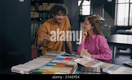 Multiracial couple buyers choosing fabric samples collection buying cloth in atelier Arabian Indian man salesman fashion designer consult Caucasian Stock Photo