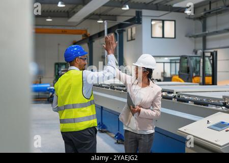 Female manager engineer giving high five to industry worker in manufacture factory. Stock Photo