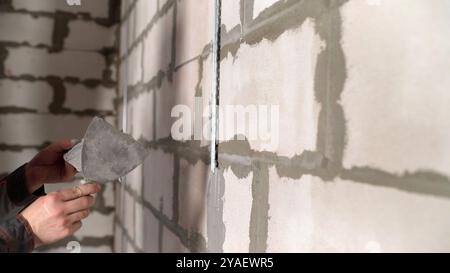 Construction worker applying plaster on white brick wall using trowel. Stock Photo