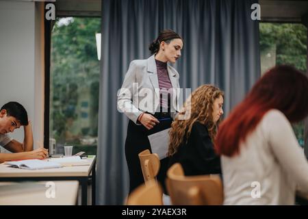 Teacher assisting students during classroom test in modern setting Stock Photo