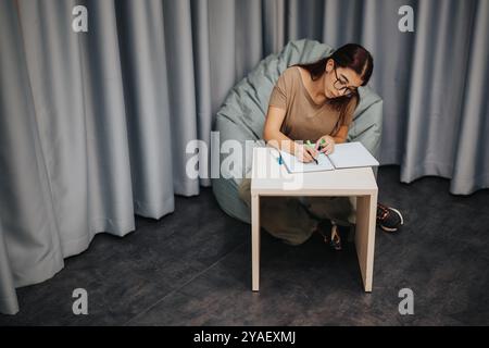 Focused high school student writing in notebook at small desk Stock Photo