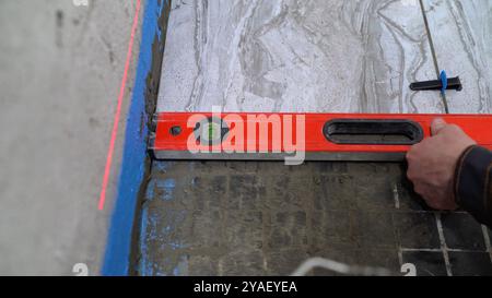 Construction worker using spirit level while laying tile. Stock Photo