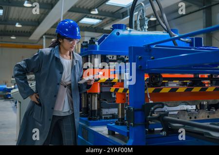 Indian woman engineer working in a production line, examining automated machinery work and writing down a planning checklist. Stock Photo