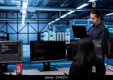 Computer scientist in data center using diagnostic tools and system monitoring software to identify root cause of errors. IT specialist in server farm establishment repairing equipment Stock Photo
