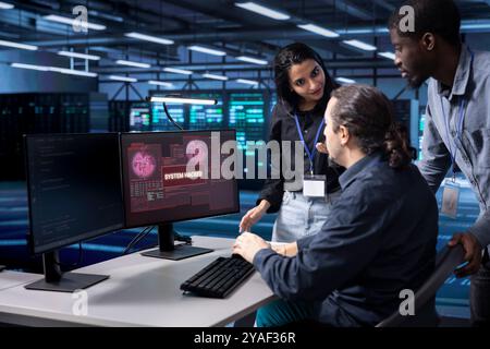 Diverse colleagues in server farm trying to protect gear from hacker stealing information. Multiethnic staff members in data center trying to fix security breach alert caused by virus Stock Photo