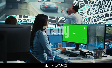 Indian employee follows order shipment next to a greenscreen on pc, communicating gps coordinates on satellite map for courier trying to avoid traffic. Cargo delivery agency. Camera B. Stock Photo