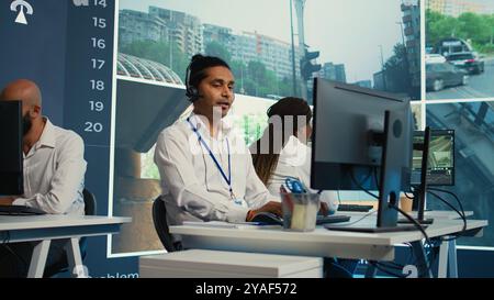 Indian employee communicating satellite map directions in observation room, monitoring traffic around the city via CCTV security system. Young man works with video surveillance data. Camera B. Stock Photo