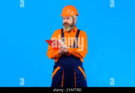 Male builder, architect or inspector with clipboard. Bearded handyman in overalls and safety hard hat writing notes on clipboard, making list of const Stock Photo