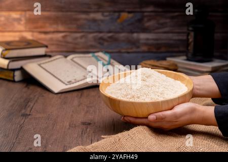 Holy Quran and a grain of rice in a wooden bowl in the sack on a wooden table, Islamic zakat concept. Muslims to help the poor and needy. Conceptual s Stock Photo