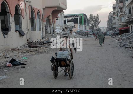 Gaza. 13th Oct, 2024. Palestinians walk on a street with buildings destroyed by Israeli strikes in the southern Gaza Strip city of Khan Younis, on Oct. 13, 2024. Credit: Rizek Abdeljawad/Xinhua/Alamy Live News Stock Photo