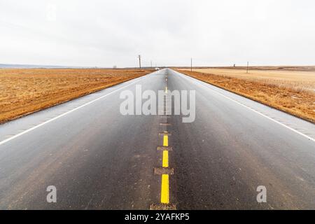 Wide open wet highway stretching into the horizon through flat brown fields under an overcast sky in Drumheller Canada Stock Photo