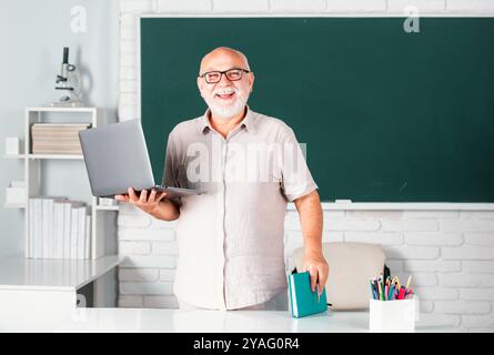 Portrait of mature teacher or tutor professor working at table in college or high school. Elderly education and retired knowledge concept. Stock Photo