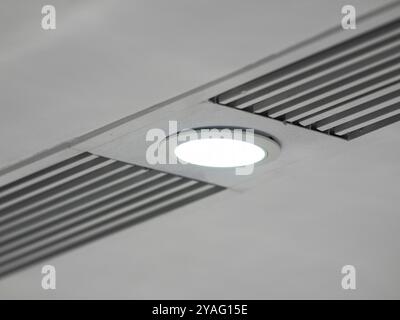 white ceiling with a poorly  mounted built-in round led light in a panel with vents, close up details. Stock Photo