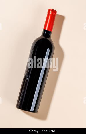 A red wine bottle lying horizontally on a bold beige background with ample copy space, creating a striking minimalist composition Stock Photo