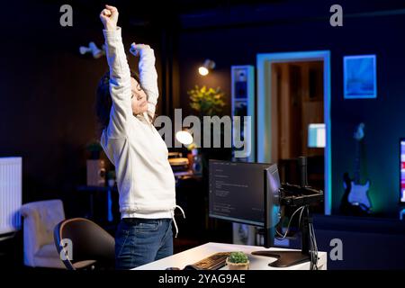 Developer doing software quality assurance, stretching after reading source code, feeling tired. IT admin relaxing muscles after inspecting coding to fix potential issues all day Stock Photo