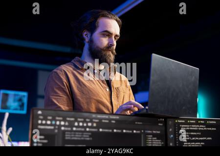 Computer scientist doing software debugging using laptop, checking glitches in lines of code displayed on PC monitors. IT specialist walking around home fixing coding issues using notebook Stock Photo