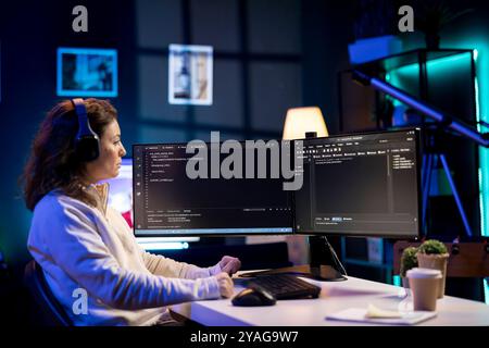 Woman listening music while doing software quality assurance, reading source code on computer screen. Admin wearing headphones enjoying podcasts and inspecting coding on desktop PC Stock Photo