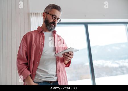 Man using smart thermostat, adjusting, lowering heating temperature at home. Smart home controlling roller blinds. Stock Photo