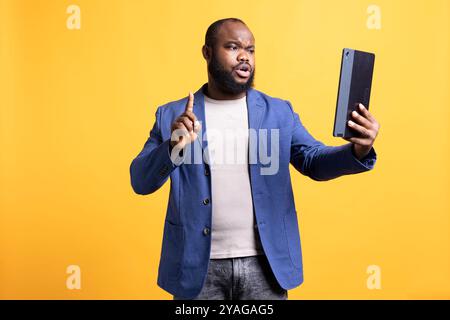 Man does no hand gesture with finger while chatting with friend during teleconference meeting using tablet, studio background. Person showing disagreeing sign, protesting mate idea during videocall Stock Photo