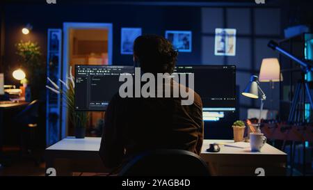 Software engineer writes binary code scripts on computer and drinks coffee. IT specialist in home office enjoying hot beverage while using programming to safeguard consumer data, camera B Stock Photo