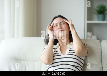 Asian woman suffering migraine sitting on a sofa at home Stock Photo