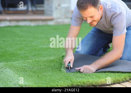 Happy man installing artificial lawn cutting a piece in the garden at home Stock Photo