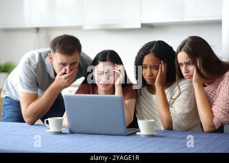 Worried interracial friends checking bad news laptop in the kitchen at home Stock Photo