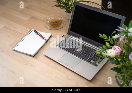 Laptop on a wooden desk, notebook, pen, tea and flowers, workplace for freelancer, study or home office, copy space, selected focus, narrow depth of f Stock Photo