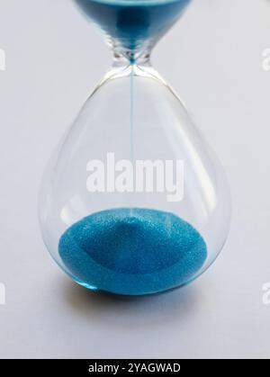 Hourglass containing blue sand isolated on white background. Concept of time passing Stock Photo