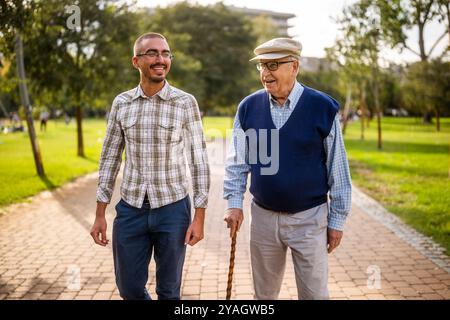Happy grandfather and grandson are walking and talking in park. Stock Photo