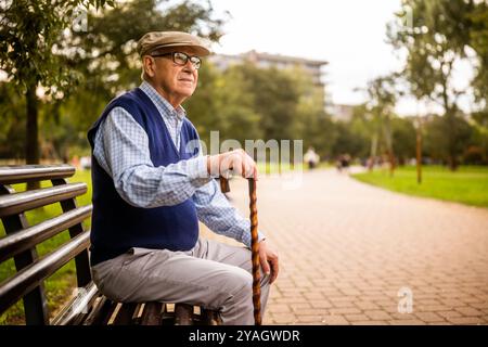 Portrait of worried senior man in park. He is sitting on bench on autumn day. Stock Photo