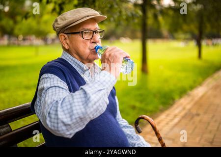 Portrait of senior man in park. He is sitting on bench, relaxing and drinking water. Stock Photo
