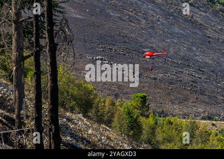 Red firefighting helicopter with water tank flies over forest fire. Abruzzo, Italy, Europe Stock Photo